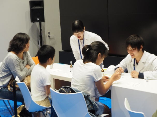 「2層のオブジェ」実験の説明をする、薬学部の田大貴さん(2年次生)=写真右と、大塚里彩さん(1年次生)