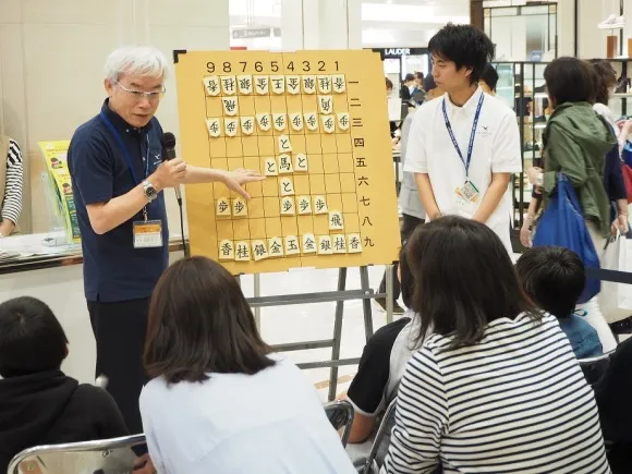 将棋の駒の動かし方について説明する河合教授と将棋部部長の高橋さん