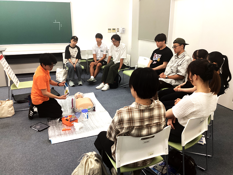 ＡＥＤの使用方法について学生インストラクターの説明を聴く課外活動団体の学生ら