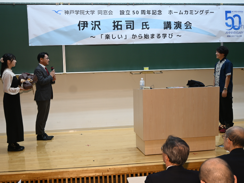 伊沢さん(右端)に御礼のあいさつをする同窓会の今岡常任幹事長(左から2人目)と花束を贈呈する心理学部生の荻野さん