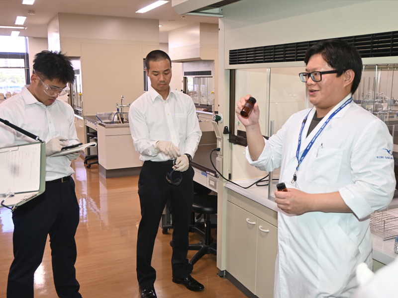 使用する薬品を示し、基礎実験の説明をする村上助教(右端)