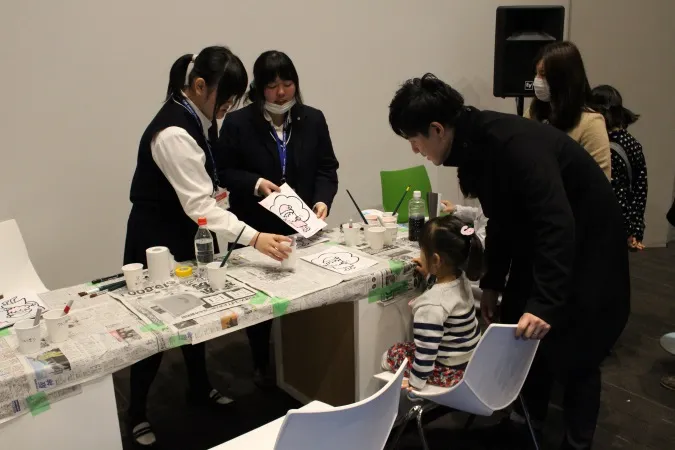 色が変わるぬり絵の説明をする附属高校の都地くるみさんと田中理子さん