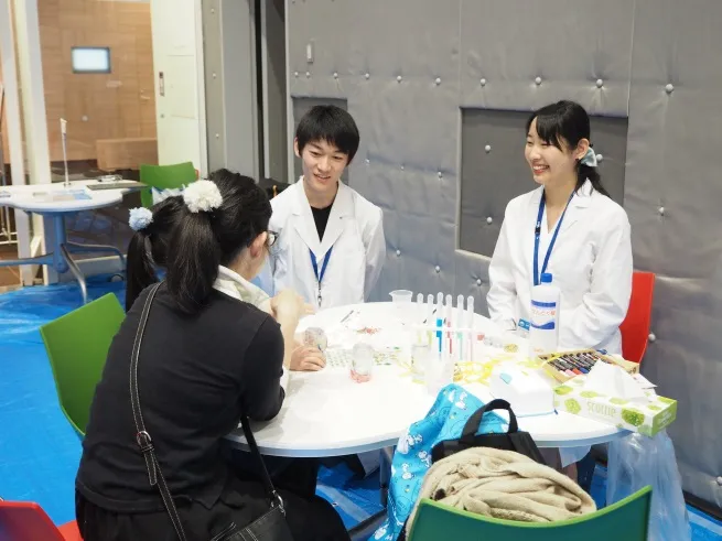 「人工イクラのスノードームづくり」の説明をする、薬学部の村岡咲季さん(4年次生)=写真右と、佐藤翔輝さん(2年次生)