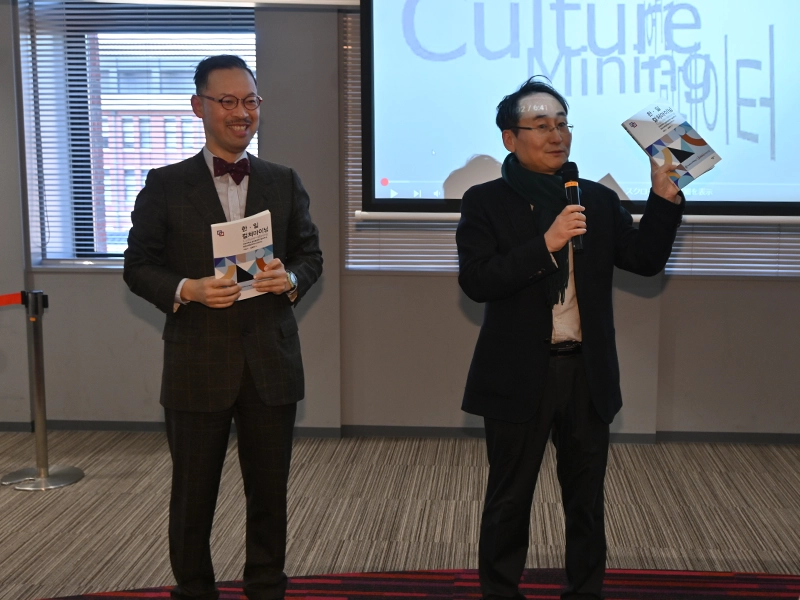 「韓日カルチャーマイニング」の書籍を持って開会あいさつする岡部所長(左)とイ・ジュンソ教授