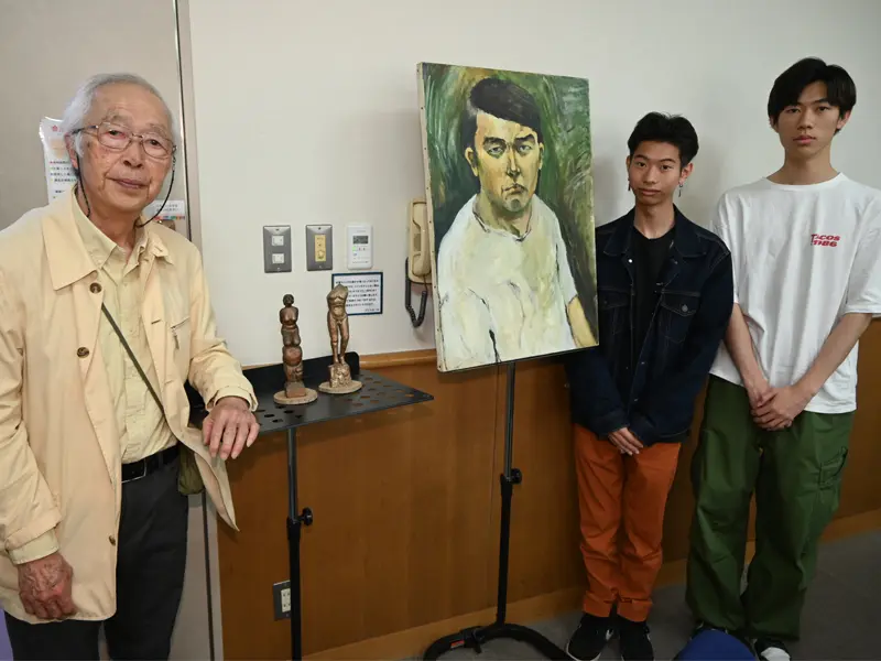田中さんがかつて描いた自画像の横で記念撮影する(右から)高瀬さんと国屋さん