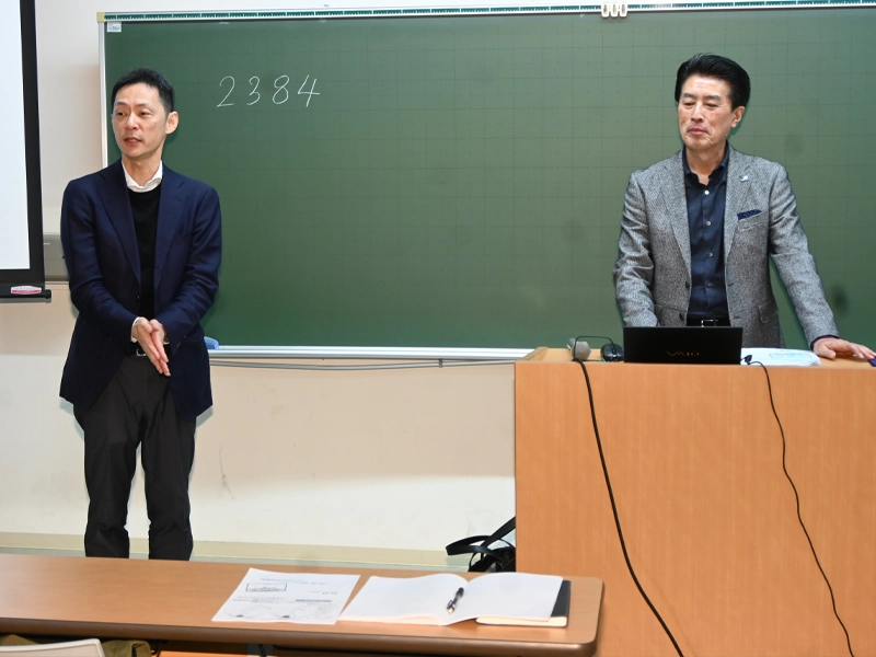 桑原会長(右)を紹介する経営学部の小川賢教授