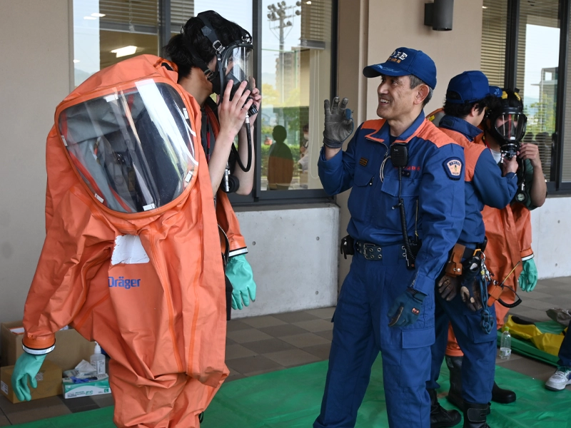 「気分はいかが?」。防護服と防災マスクを装着した学生は感想を聞かれ、「……」