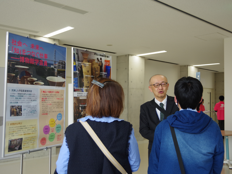 博物館学芸員課程を紹介するパネルの前で来場者に説明する矢嶋巌教授