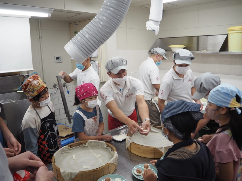 子どもたちに豚饅頭の包み方を説明