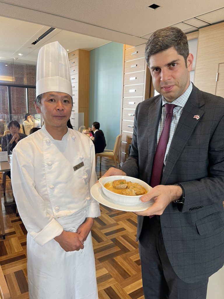 学内のレストラン「ジョリポー」で民族料理「シュクメルリ」を手にするレジャバ大使(同大使提供)
