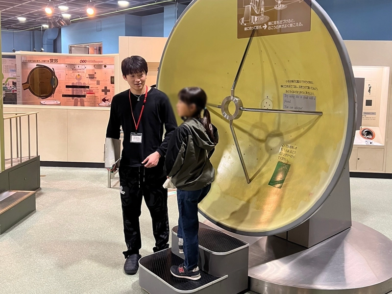 音の反射を利用したパラボラアンテナの働きを体験する小学生とサポートする江田ゼミ生