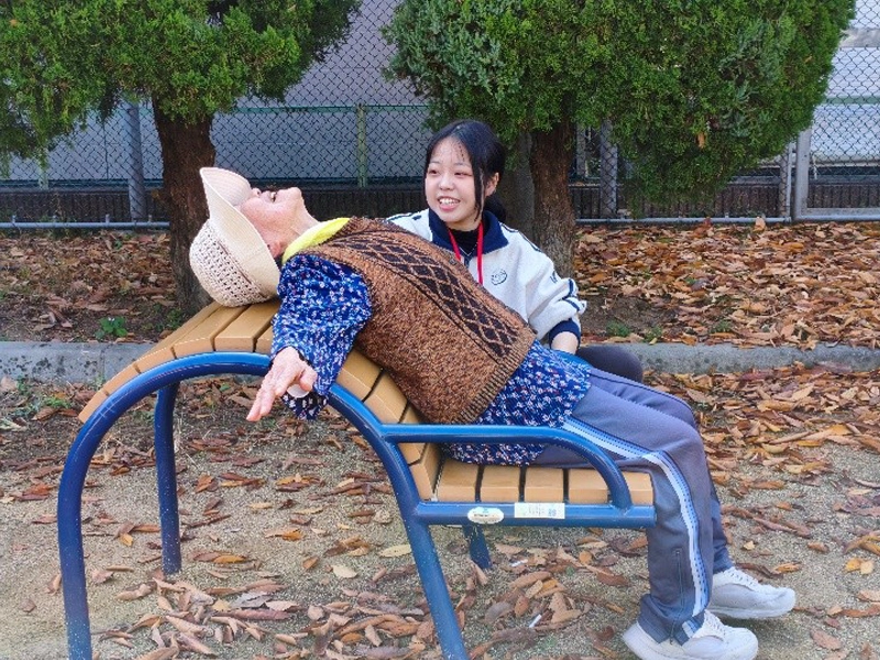 背中伸ばしベンチを使った運動の指導を行う学生