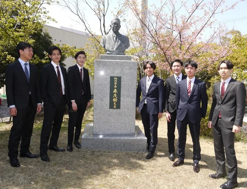 森茂樹博士の胸像の前で記念撮影する卒業生ら