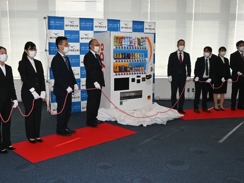 地域貢献型自動販売機を除幕し、記念撮影する関係者ら
